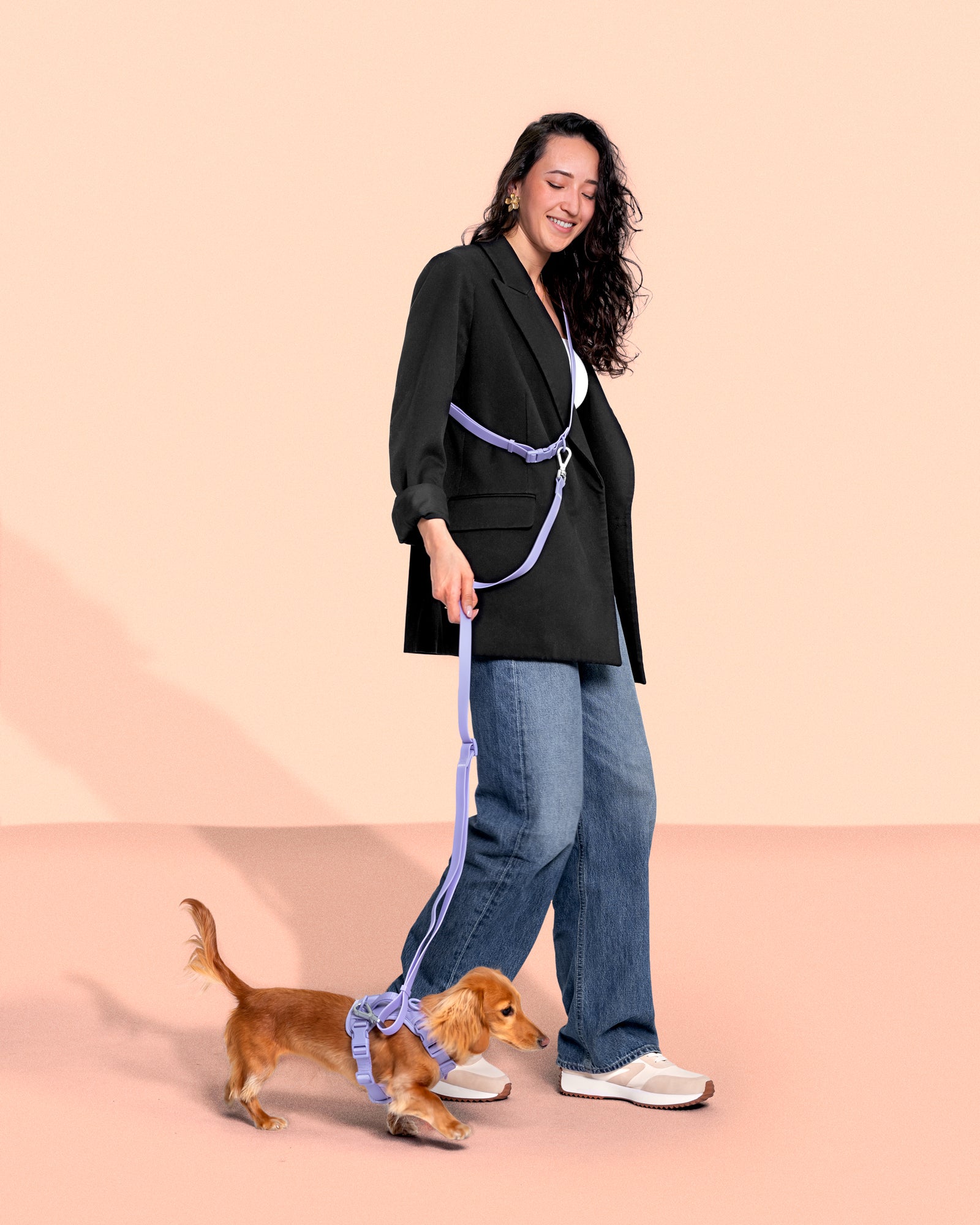 women smiling and walking in a studio colored backdrop with the hands free leash attached to a small dog with a harness
