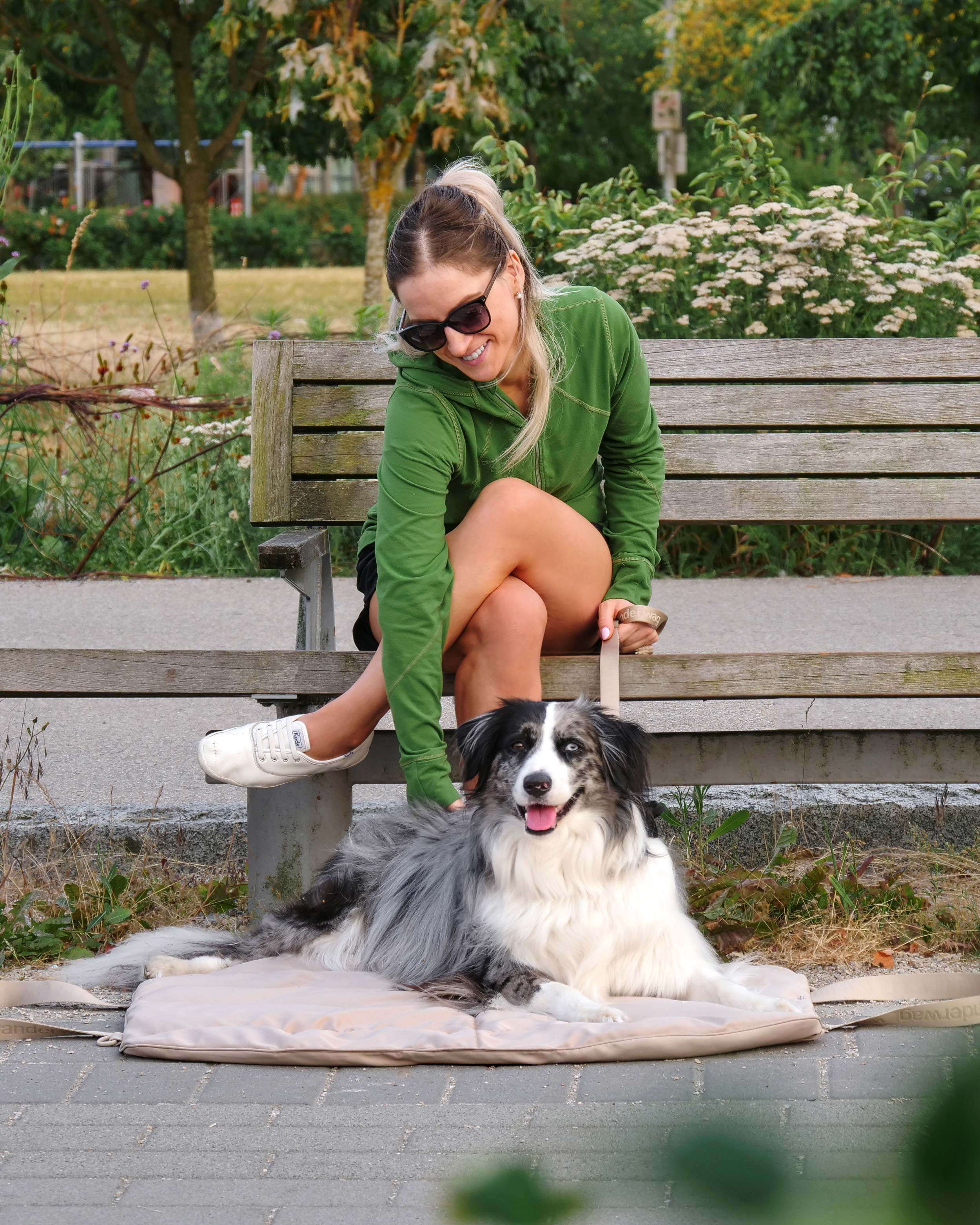 women on a park bench leaning over to pet dog laying on the wanderwag tote bed
